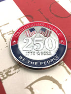 A round commemorative challenge coin celebrating the United States 250th anniversary, featuring crossed American flags, '250' in the center, and 'UNITED STATES OF AMERICA' and 'WE THE PEOPLE' in red, white, and blue sections.