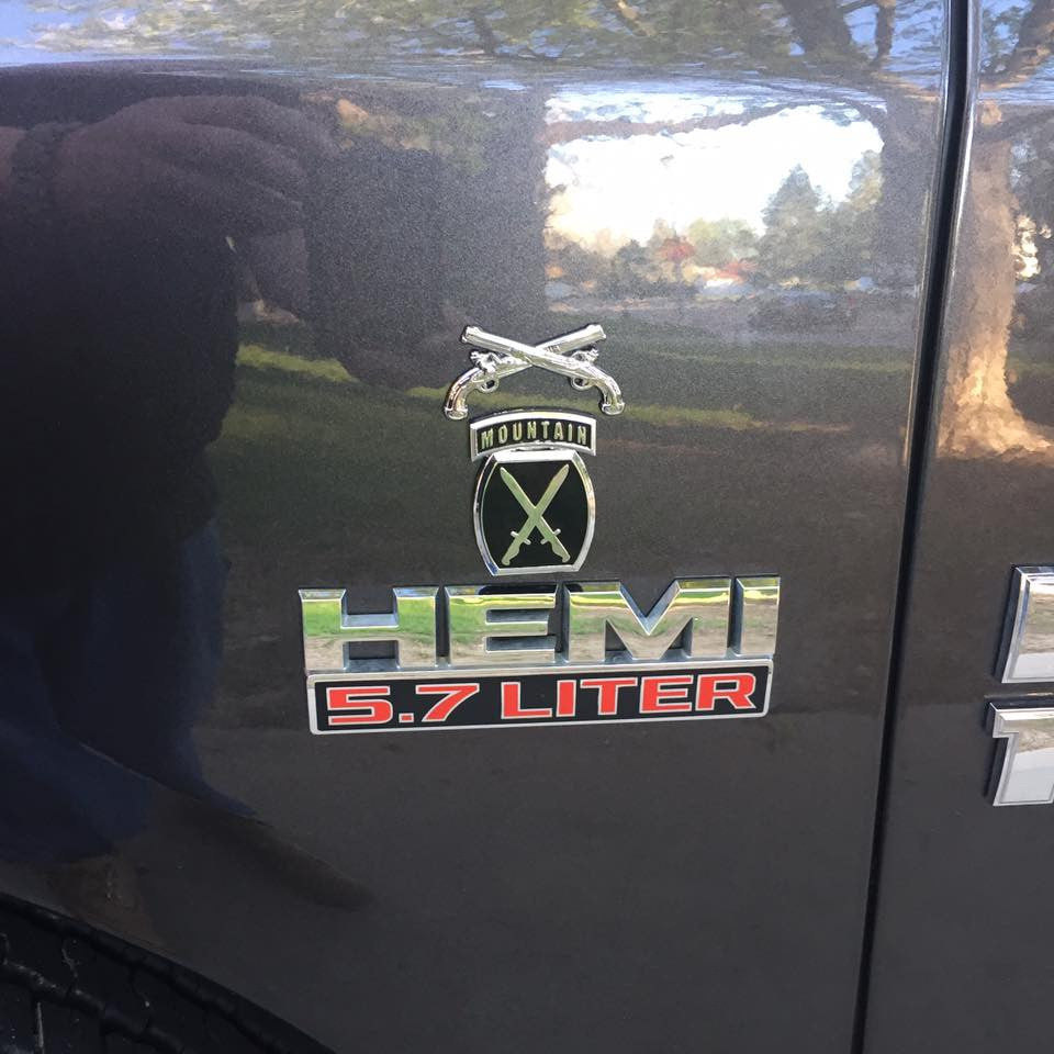 A chrome plated, zinc alloy Military Police Corps Insignia with a cross pistols design, attached to a vehicle.