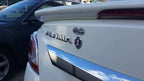 A Combat Action Badge attached to the rear of a white vehicle, featuring chrome plating and a military emblem.